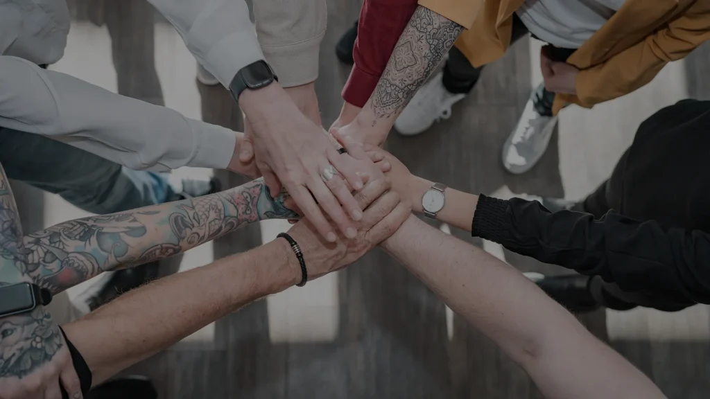 Mehrere Teammitglieder legen im Kreis die Hände übereinander – Symbol für Zusammenhalt und Gemeinschaft